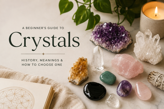 A flat lay of assorted crystals including amethyst, clear quartz, rose quartz, citrine, green aventurine and black obsidian beside a lit candle, sage bundle and journal