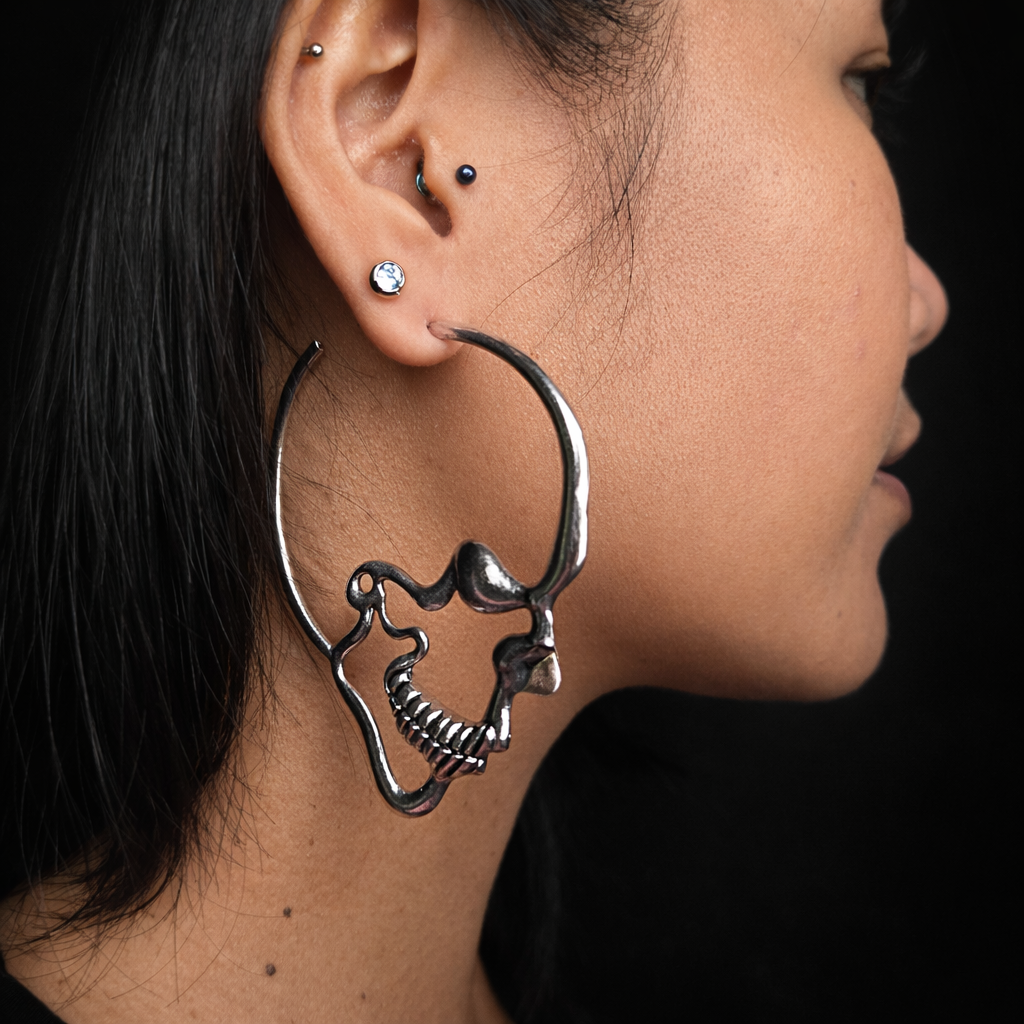 Oversized silver skull hoop earrings, modelled on ear.