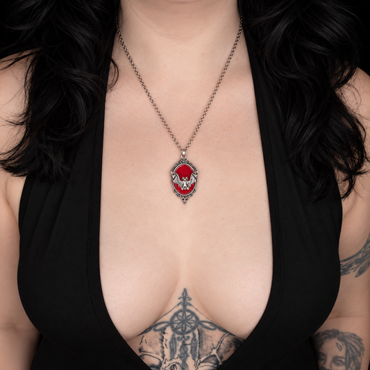 Model wearing the Bloodhunt necklace, featuring an ornate silver-tone oval pendant with a red centre and decorative bat motif on a chain.