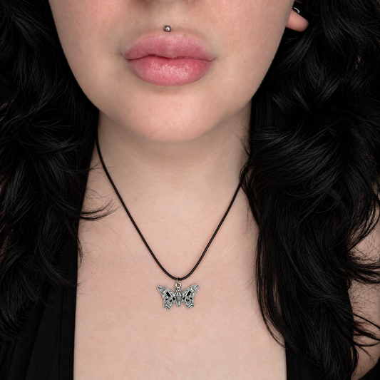 Model wearing the Beauty Sleep necklace, featuring a small detailed silver-tone butterfly pendant on a black cord necklace.