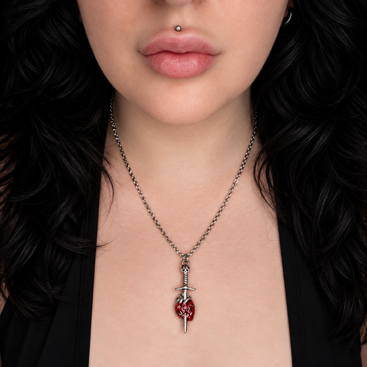 Model wearing the Funeral of Hearts necklace, featuring a silver-tone sword pendant piercing a detailed red anatomical heart on a chain.