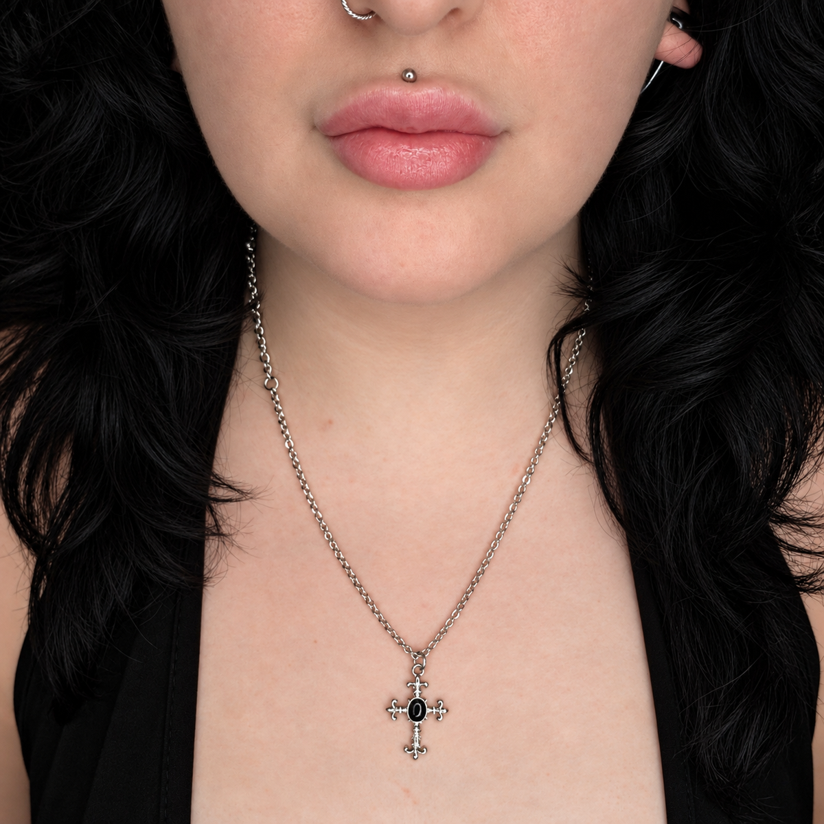 Model wearing the Obsidian Knight necklace, featuring a small ornate silver-tone cross pendant with a central oval black stone on a chain.