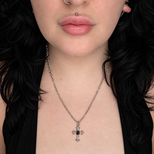 Model wearing the Obsidian Knight necklace, featuring a small ornate silver-tone cross pendant with a central oval black stone on a chain.
