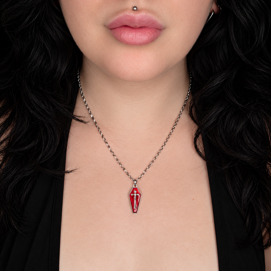 Model wearing the Sunlights Solace necklace, featuring a small red coffin-shaped pendant with a silver-tone cross design on a chain.