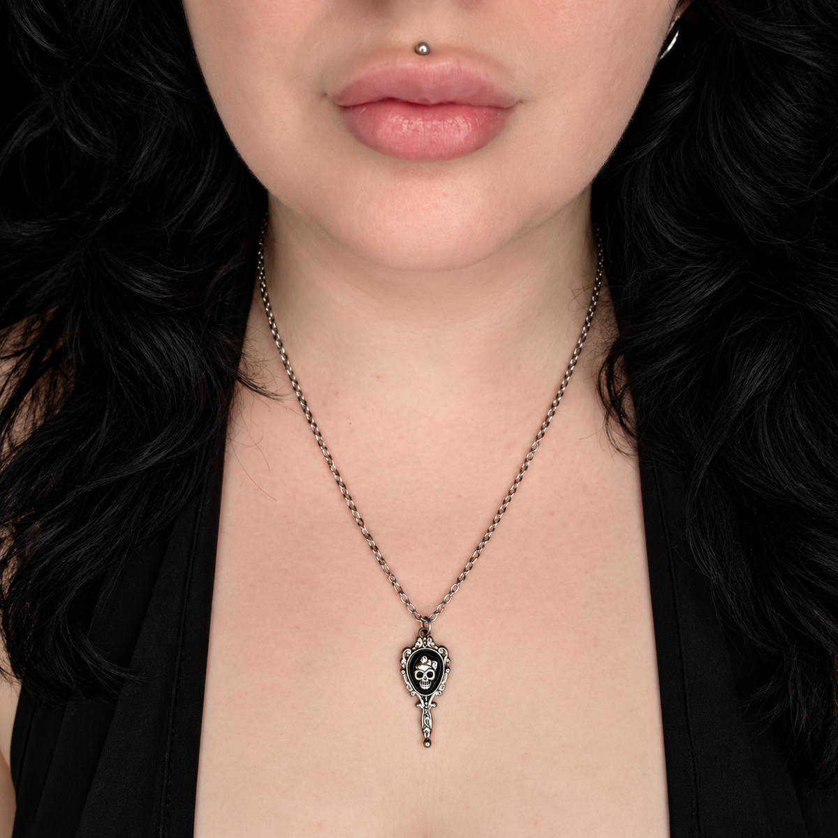 Model wearing the If Looks Could Kill necklace, featuring a small ornate silver-tone hand mirror pendant with a black skull design in the centre on a chain.