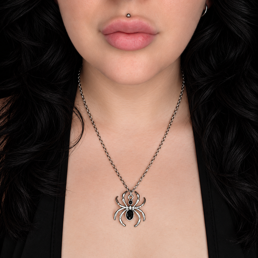 Model wearing the Onyx Arachnid necklace, featuring a large silver-tone spider pendant with a black oval centre on a chain.