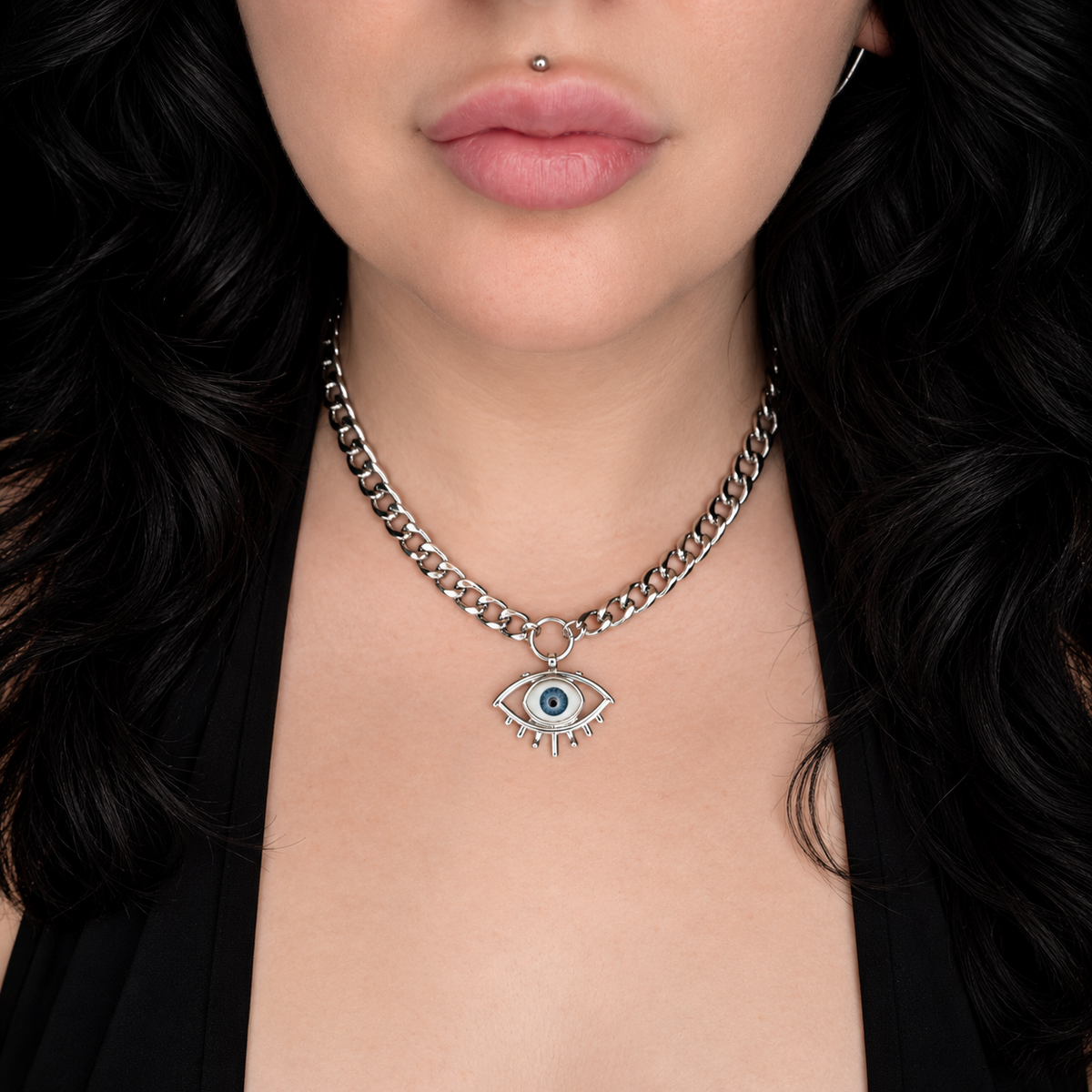 Model wearing the All Seeing necklace, featuring a silver-tone eye pendant with a blue iris and eyelash detailing on a chunky silver-tone chain.