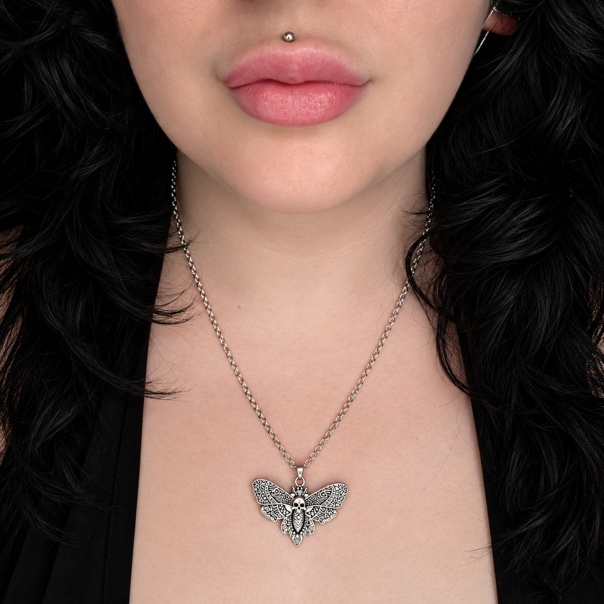 Model wearing the Moirai Wings necklace, featuring a detailed silver-tone moth pendant with spread patterned wings on a chain.