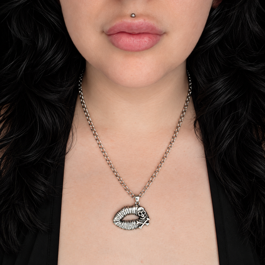 Model wearing the Poisonous Kiss necklace, featuring a silver-tone lips pendant with a small skull and crossbones detail on a chunky chain.