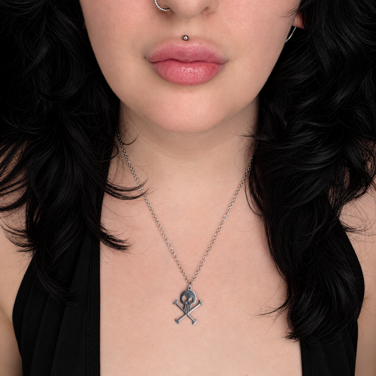 Model wearing the Punished Dolls necklace, featuring a small silver-tone skull and crossed bones pendant on a delicate chain.